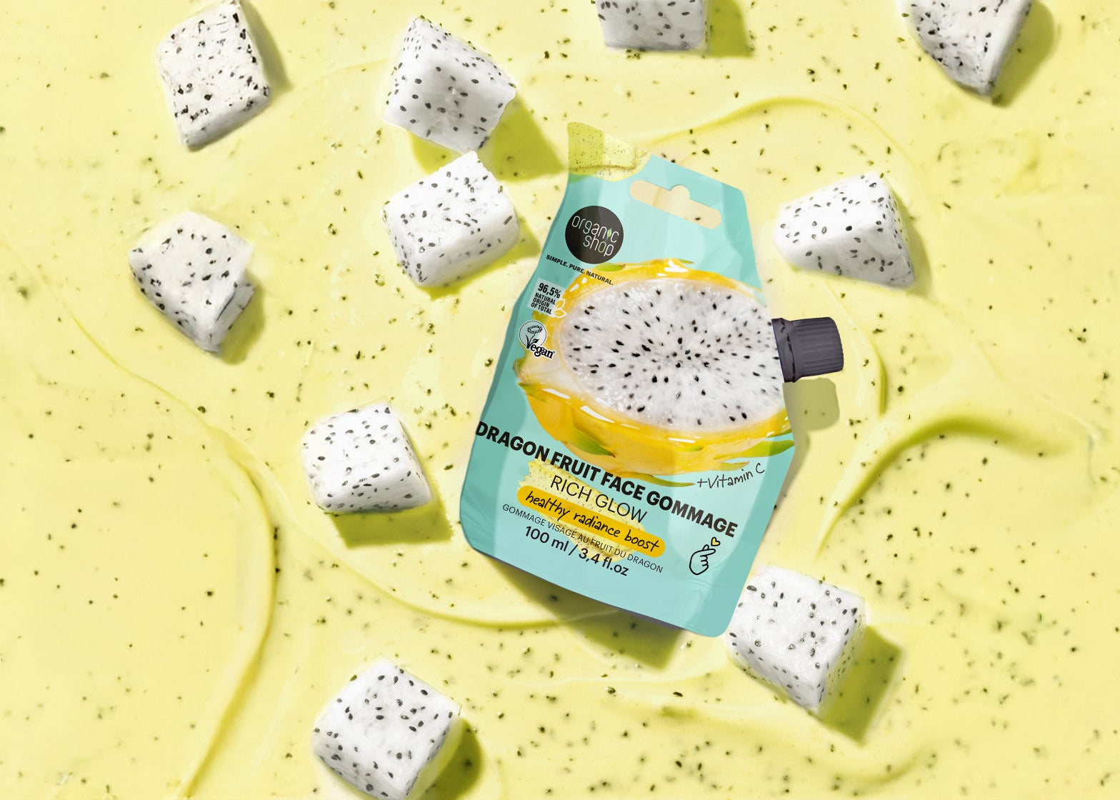 Packaged dragon fruit face exfoliant on a yellow background with dragon fruit pieces.