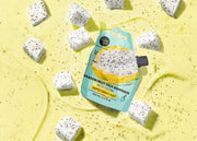 Packaged dragon fruit face exfoliant on a yellow background with dragon fruit pieces.